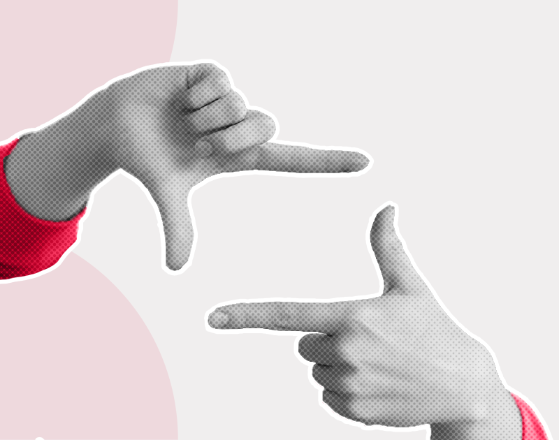 Two hands in red sleeves form a rectangular frame against a light gray and pink background, conveying a concept of focus or creativity.