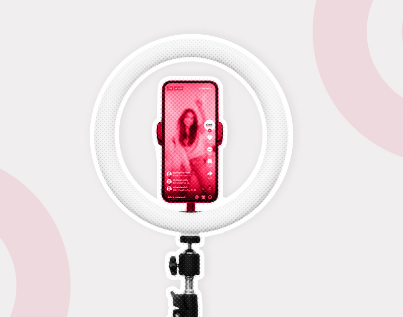 A smartphone mounted on a tripod is framed by a glowing ring light, displaying a livestream with a person in red hues, conveying an energetic online presence.