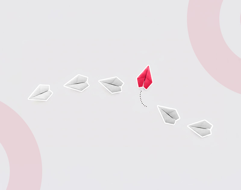 Five gray paper planes and one red plane on a light background. The red plane veers upward, symbolizing innovation and uniqueness.